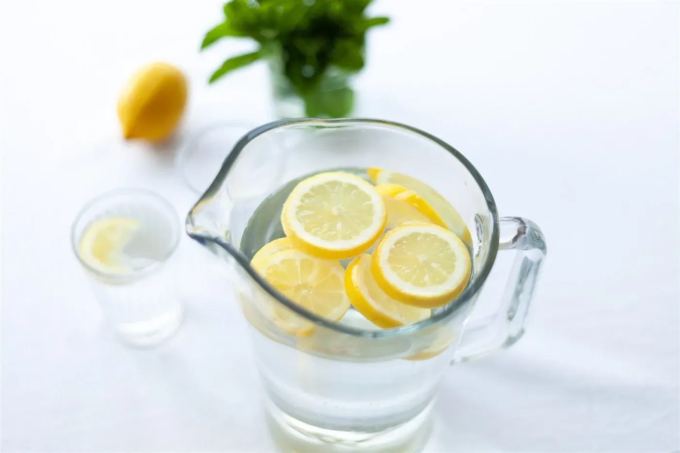 Bình nước có lát chanh và ly nước chanh trên bàn trắng