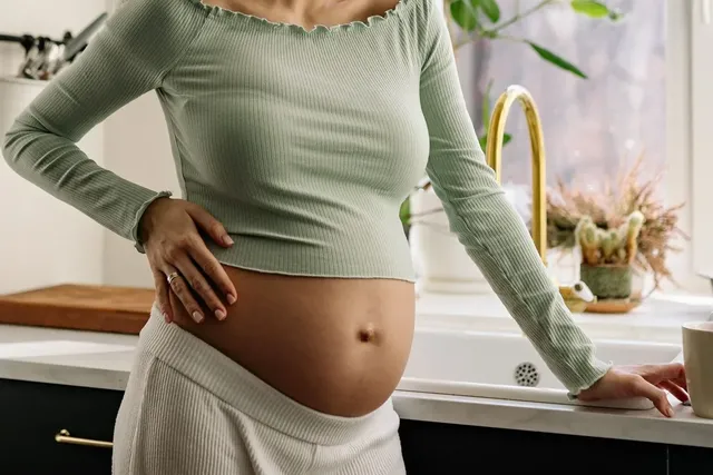 Người mẹ mang thai đứng trong bếp, tay đặt lên bụng, minh họa chăm sóc răng miệng khi mang thai